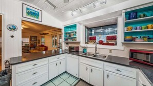 A kitchen with white cabinets, a black countertop, a window with a view, and a microwave. - Su Casa 5BR Beachfront Cottage in Indian Rocks (Indian Rocks Beach)