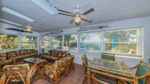 A sunroom with a ceiling fan, large windows, wicker furniture, and a glass table. - Su Casa 5BR Beachfront Cottage in Indian Rocks (Indian Rocks Beach)