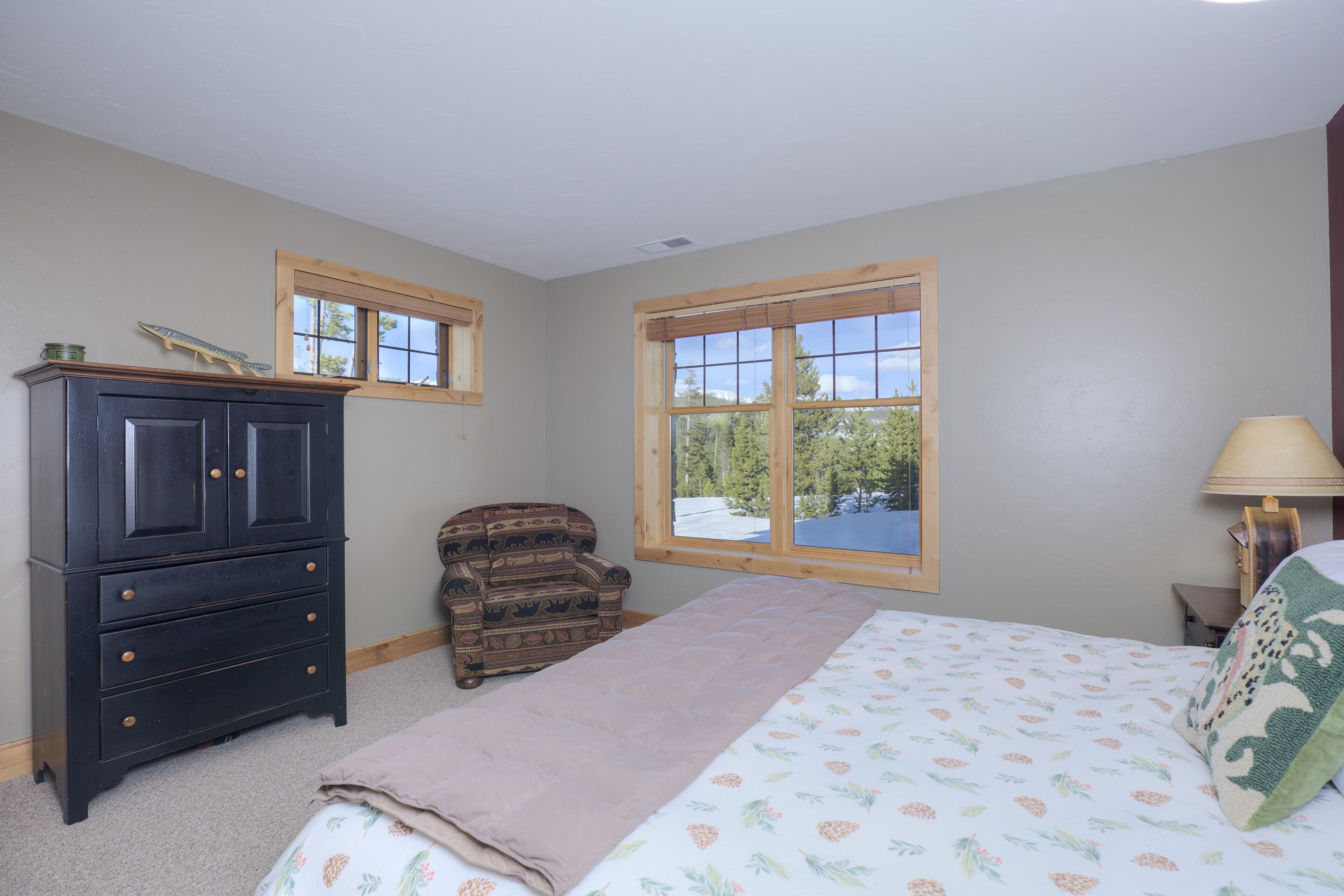 A bedroom with a bed, dresser, chair, and windows with a view of trees.