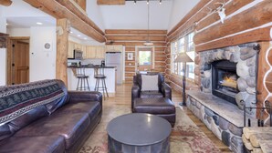 A log cabin interior with a stone fireplace, leather furniture, and a kitchen area. - Ski-In/Ski-Out Powder Ridge Cabin In Beautiful Big Sky (Big Sky)