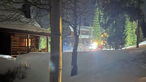 A snow-covered landscape with a wooden cabin and a building in the background. - Ski-In/Ski-Out Powder Ridge Cabin In Beautiful Big Sky (Big Sky)