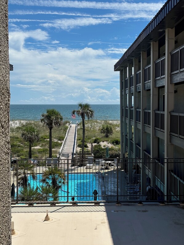 A pool area with a view of the ocean, a wooden deck, and a building with balconies.