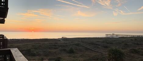 A sunset view from a balcony overlooking a beach with a wooden pier extending into the water.