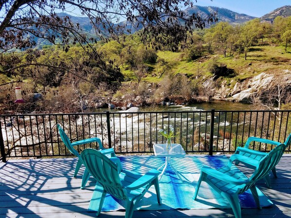 Terraza con sillas turquesa y una mesa, con vista a un río y montañas.