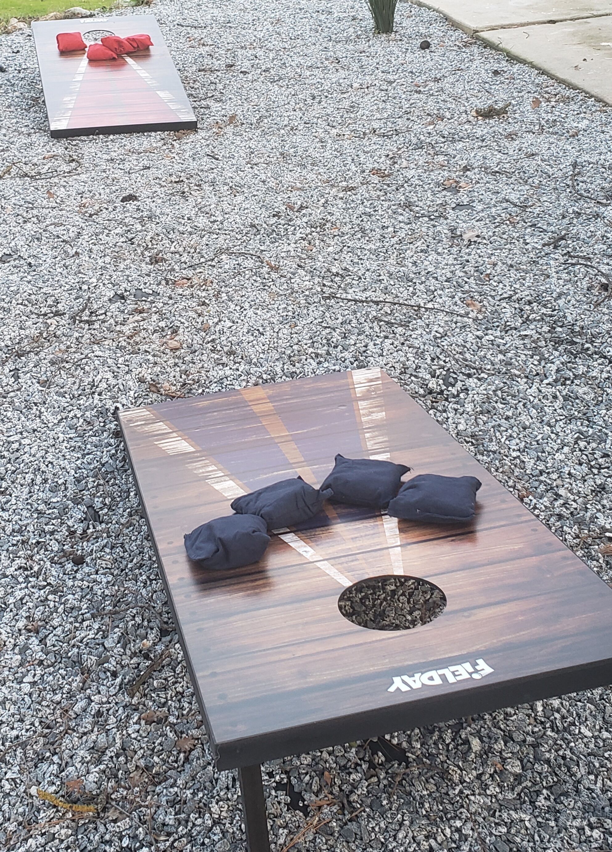 A wooden board game on a gravel surface with black cushions and a hole in the center.