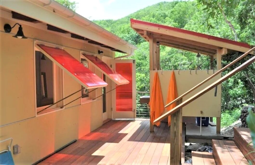 A covered outdoor deck with a wooden floor, a red awning, and a view of a forested hillside.