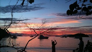 Ein Sonnenuntergang über einem ruhigen Meer mit Booten, Silhouetten von Menschen und einer fernen Insel.