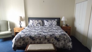 A neatly arranged bedroom with a bed, bedside tables, a chair, and a wardrobe.