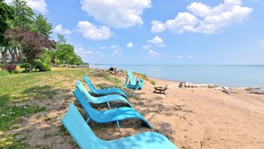 A beach with blue lounge chairs and a wooden fire pit. - Prepare to fall in love with this adorably tropical beach front property! (Kingsville)