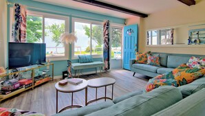 A living room with a television, seating area, and large windows. - Prepare to fall in love with this adorably tropical beach front property! (Kingsville)