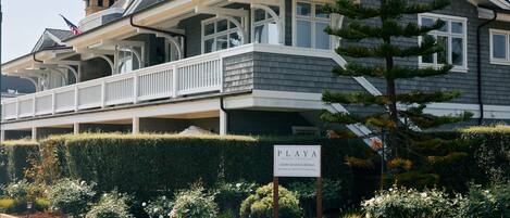 A two-story building with a balcony, a sign indicating it is a beach lodging, and a well-maintained garden with various plants and flowers.