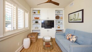 A living room with a ceiling fan, a television, a blue sofa, and a bookshelf.