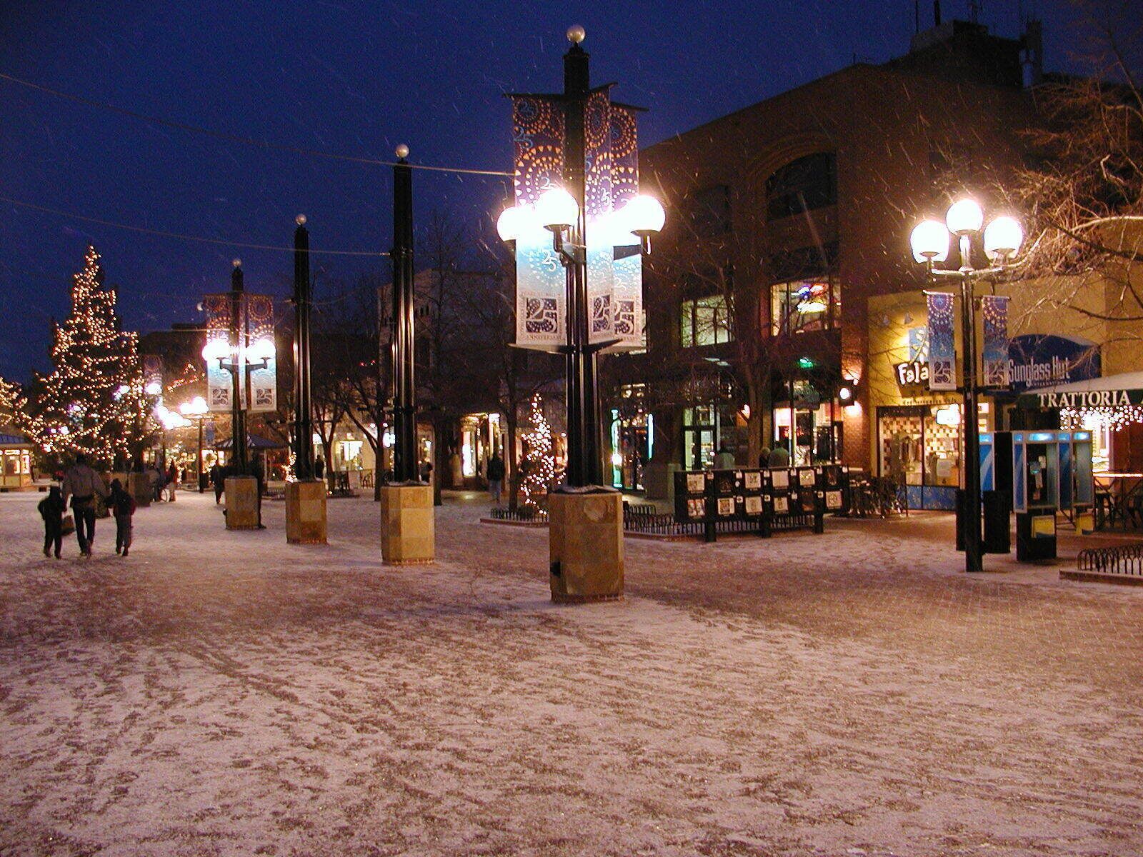 A snowy square with illuminated street lamps and a Christmas tree.