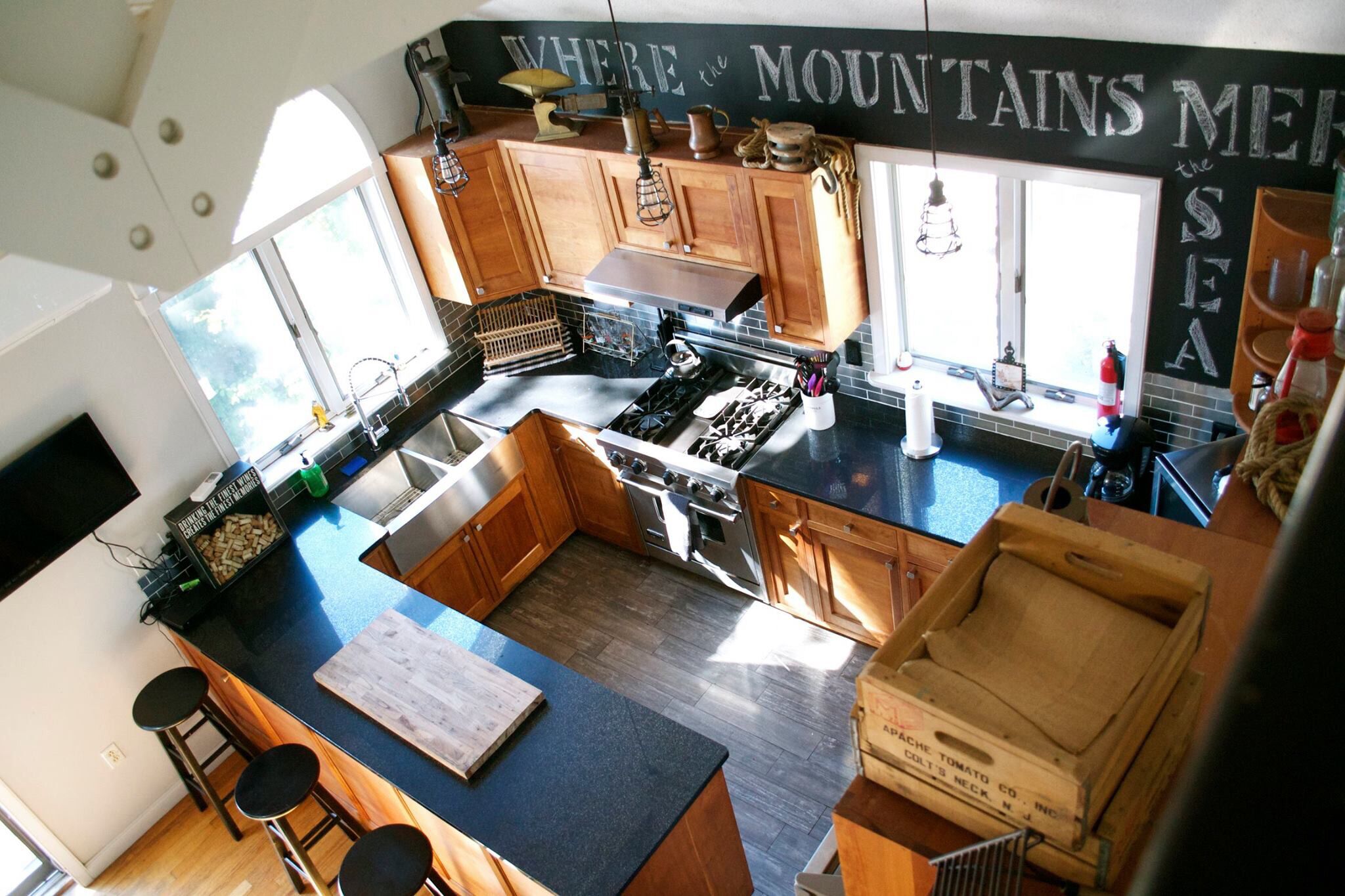 A kitchen with a large island, wooden cabinets, a gas stove, and a chalkboard with writing.