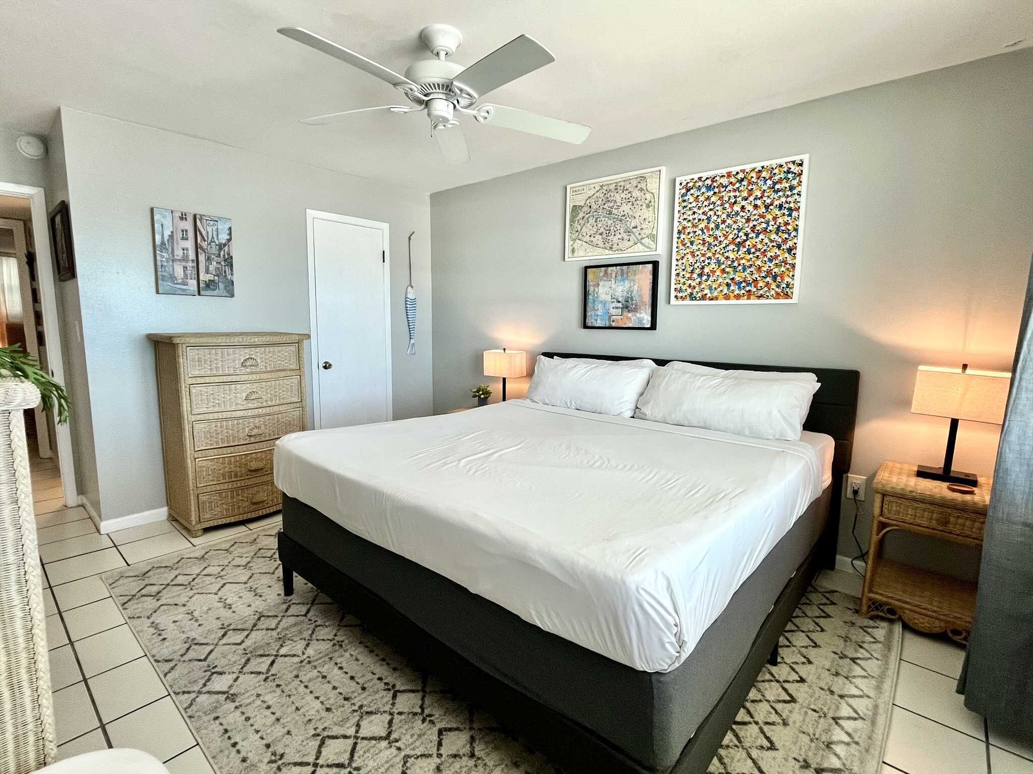 Ein Schlafzimmer mit einem Bett, einem Deckenventilator, einer Kommode und zwei Wandbildern.