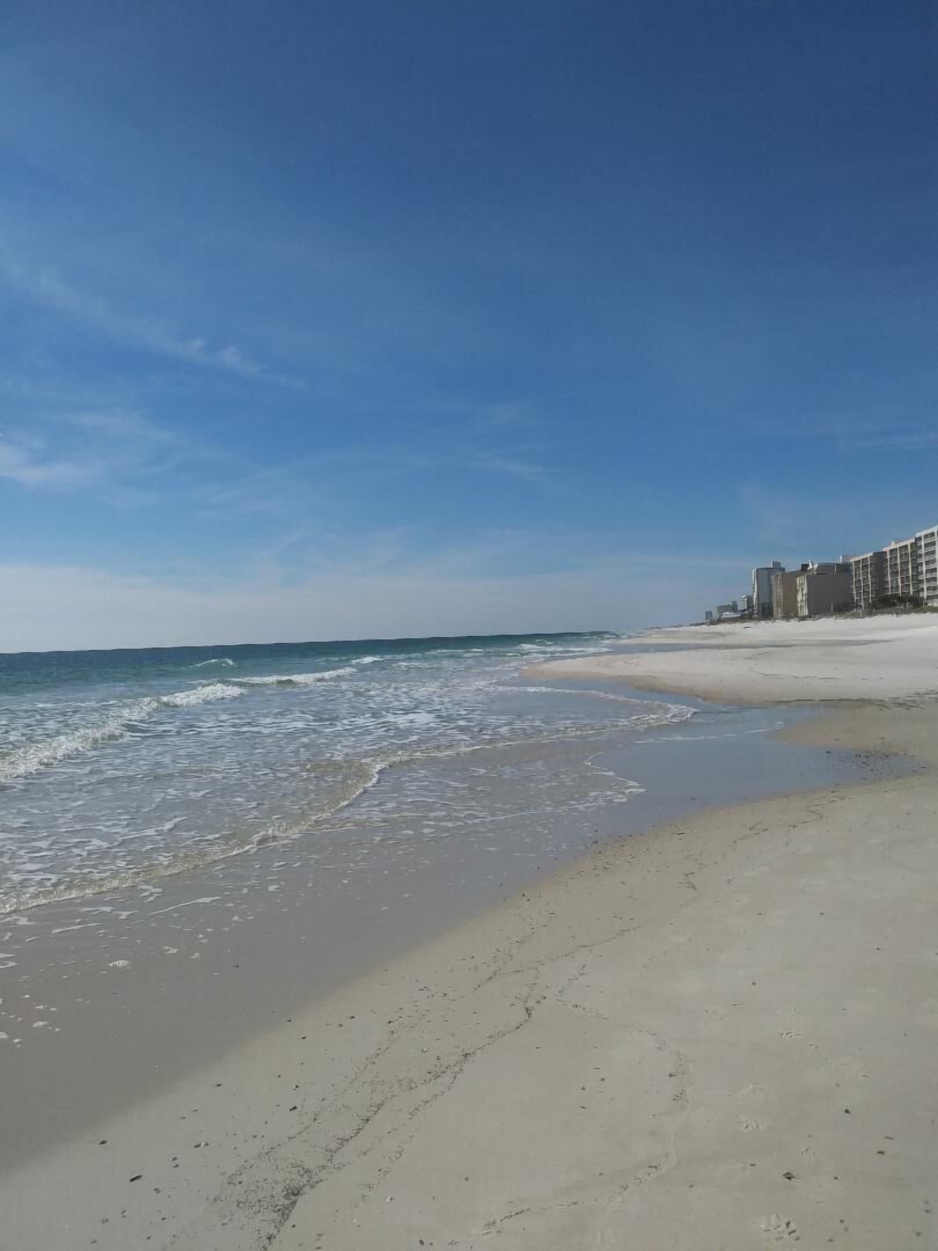 A beach with a clear sky and a building complex in the background.