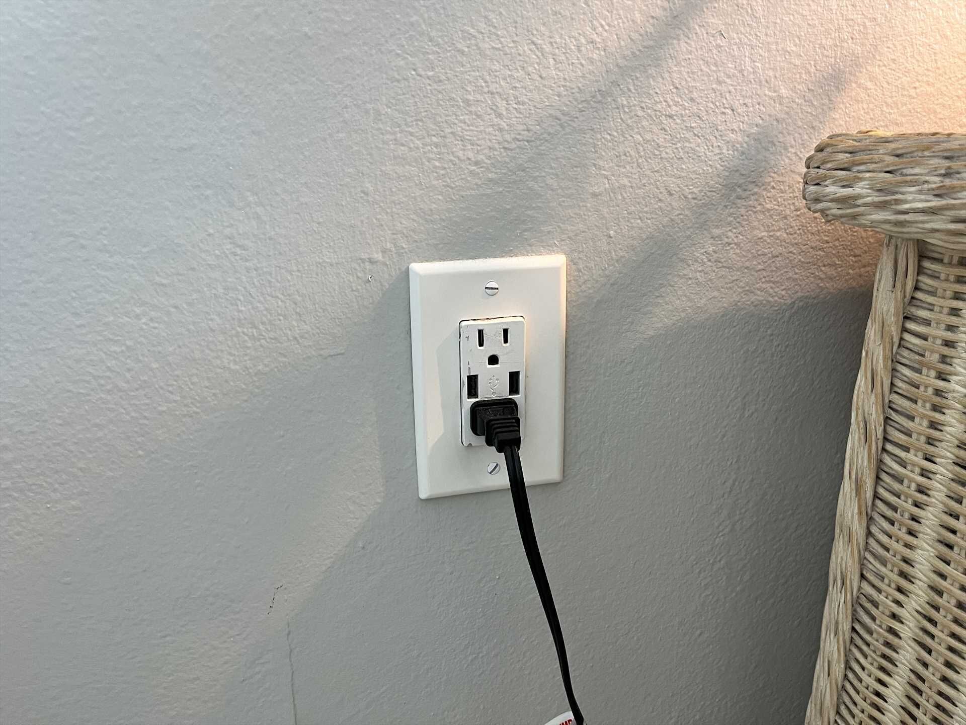 A white electrical outlet with a black cable plugged in, mounted on a textured wall.