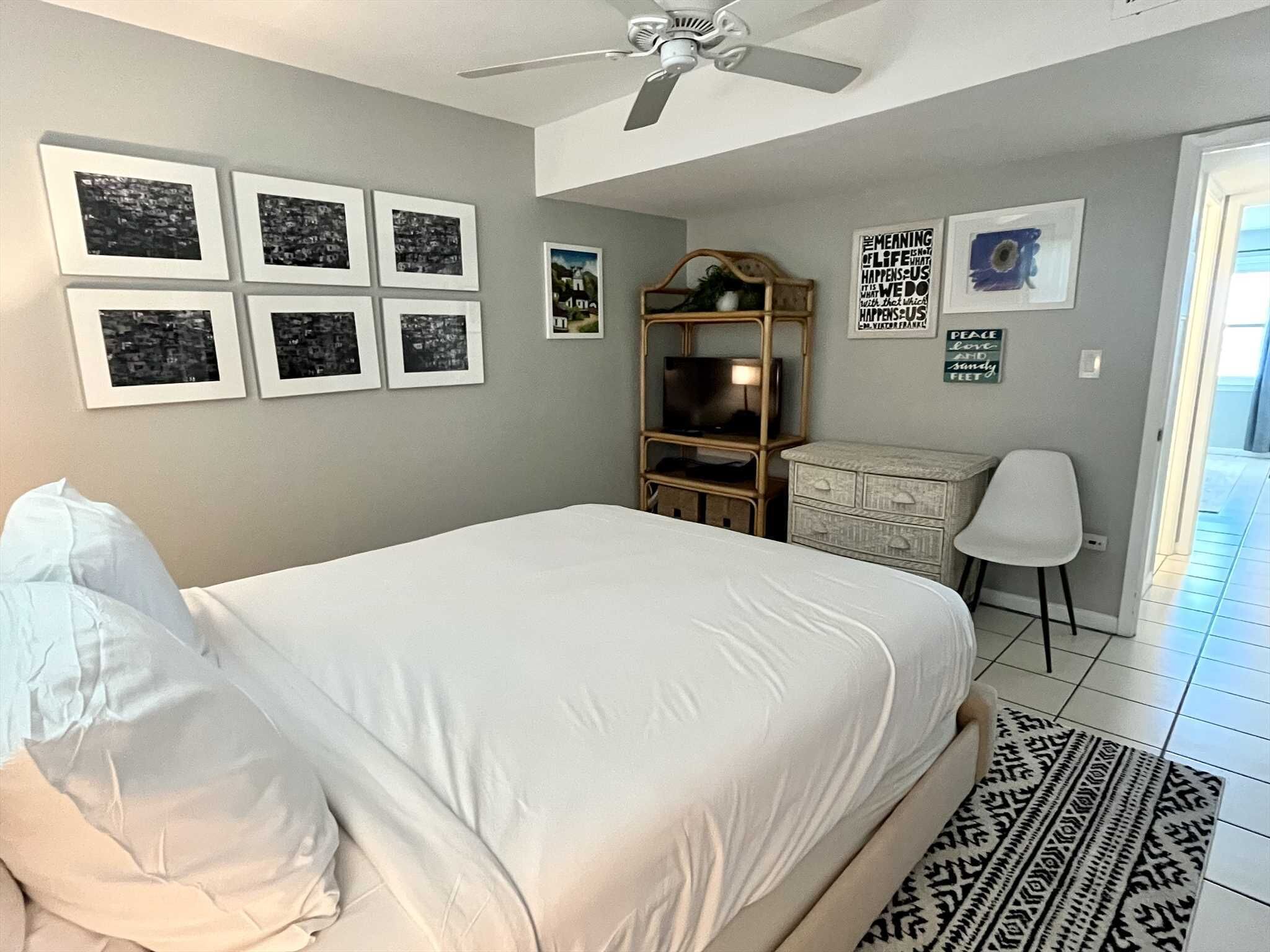 Een slaapkamer met een bed, een plafondventilator, een dressoir, een televisie en ingelijste foto's aan de muur.