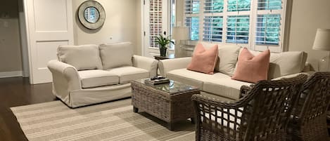 A living room with a beige sofa, two armchairs, a coffee table, and a large window with blinds.