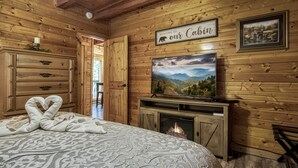Ein gemütliches Cabin-Zimmer mit Kamin, einem darüber montierten Fernseher und einem Schild mit der Aufschrift "Welcome to our Cabin".