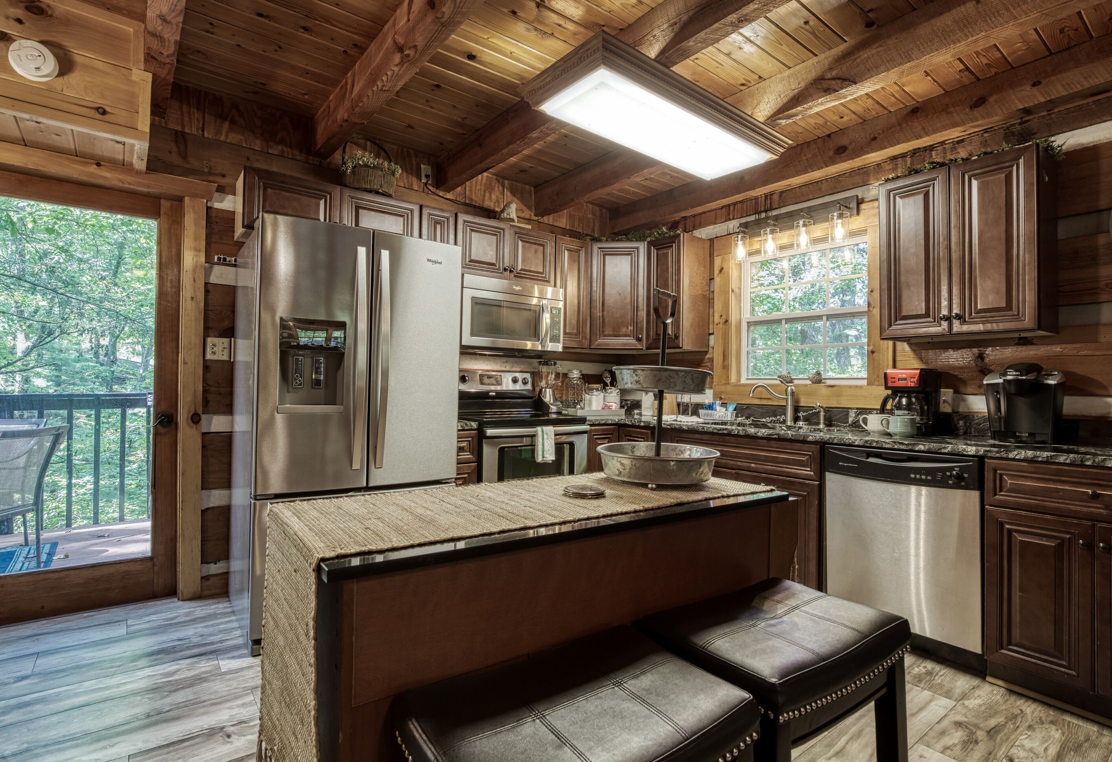 A wooden cabin kitchen with a central island, stainless steel appliances, and a view of the outdoors.