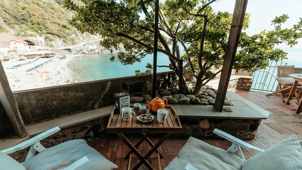 Una mesa de madera con un juego de café, dos sillas acolchadas y vistas a una playa y al océano.