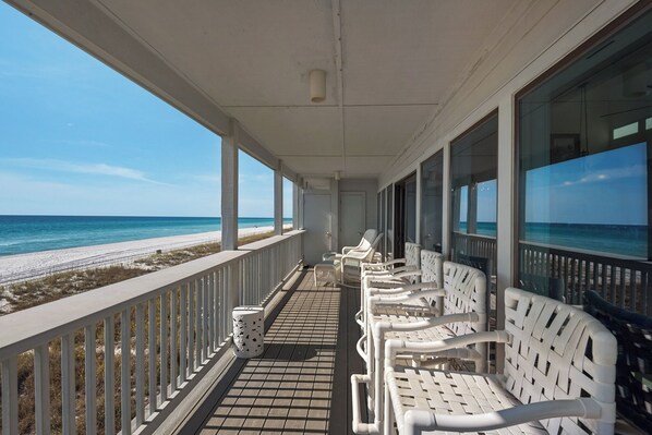 Un balcon abrité, doté de chaises en osier blanches, d’un sol carrelé et offrant une vue sur la plage et l’océan.