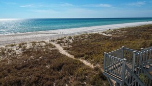 Ein Strand mit einem sandigen Pfad, der zum Wasser führt, einer Holztreppe und einem klaren, blauen Himmel.