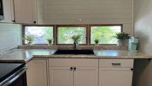 A kitchen with a granite countertop, a black sink, white cabinets, and a window with three panes.