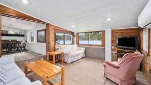 A spacious living area with a wooden floor, a sofa, a pink armchair, a wooden coffee table, and a television.