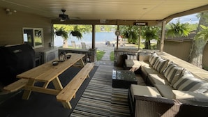 A covered outdoor seating area with a wooden table, cushioned sofas, and a view of a lake.