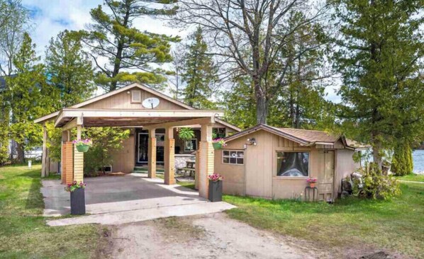 Guests can enjoy a serene setting surrounded by a well-maintained lawn and mature trees on the covered porch.