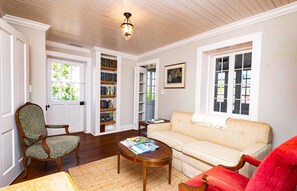 A living room with a beige sofa, a wooden coffee table, a patterned armchair, a red chair, and a bookshelf.