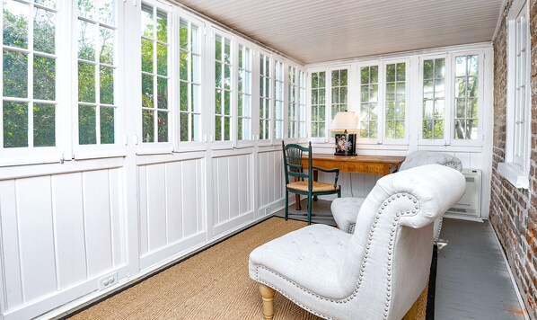 A room with large windows, a wooden table, a chair, and a lamp.