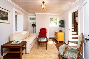 A living room with a sofa, a red armchair, a wooden coffee table, and a television on a stand.