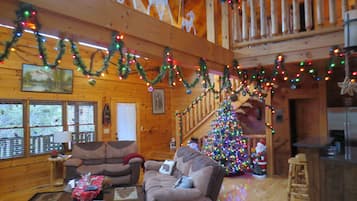 A cozy cabin interior with wooden walls, a staircase, a Christmas tree, and festive decorations.