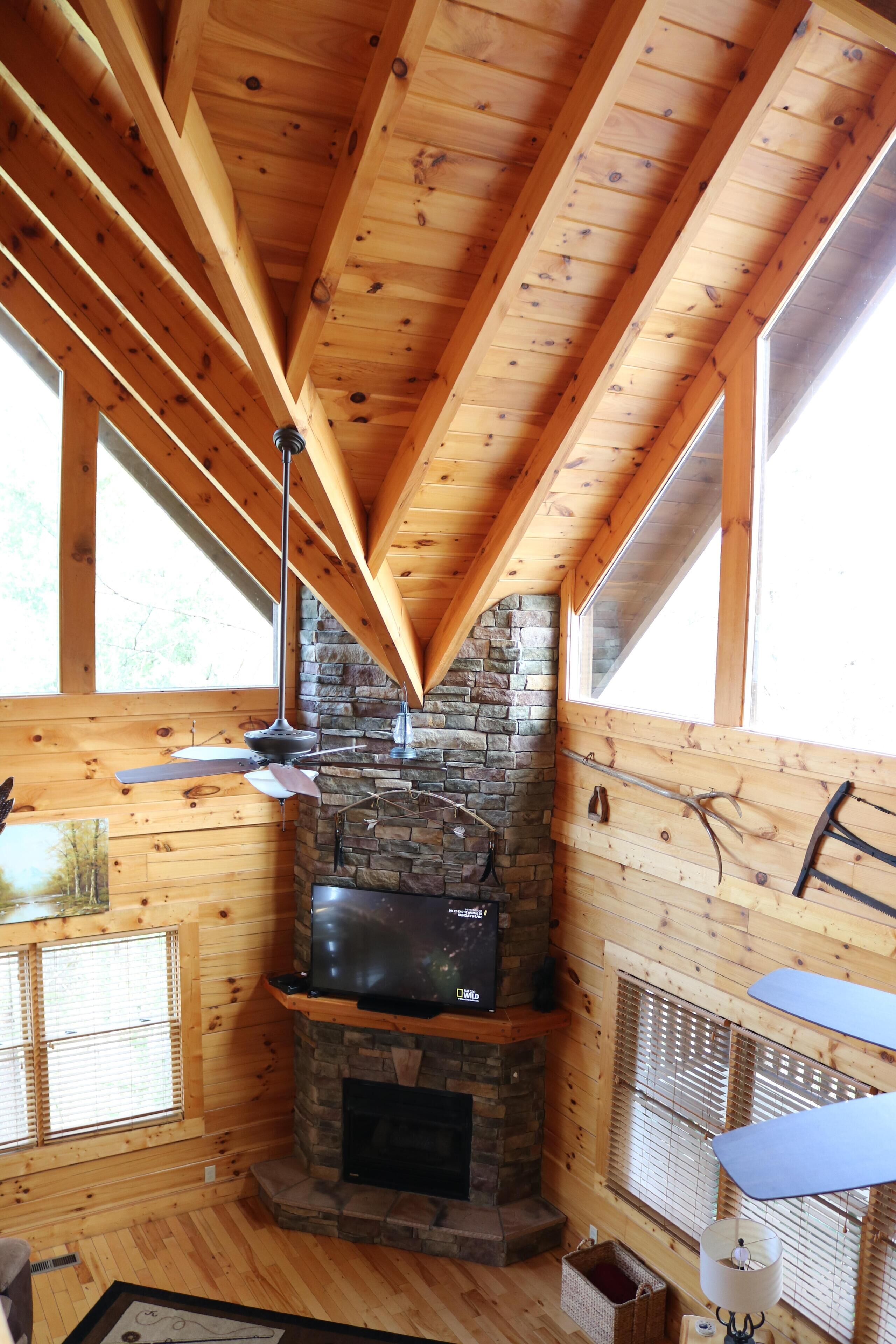 A cozy cabin interior with a stone fireplace, wooden beams, and large windows.