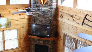 Interior acollidor d'una cabana amb una llar de pedra, bigues de fusta i grans finestres.