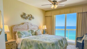 A bedroom with a bed, nightstands, a ceiling fan, and a view of the ocean. - L👀K!!! ⭐️ TOP RATED ⭐️ DIRECT BEACHFRONT Condo at Calypso + FREE Beach Chairs !!! (Panama City Beach)