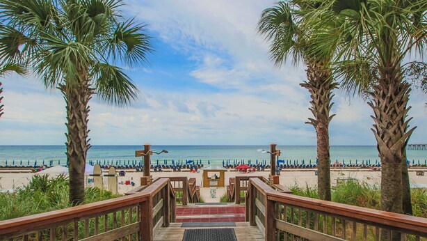 A wooden staircase leading to a beach with palm trees and umbrellas. - L👀K!!! ⭐️ TOP RATED ⭐️ DIRECT BEACHFRONT Condo at Calypso + FREE Beach Chairs !!! (Panama City Beach)