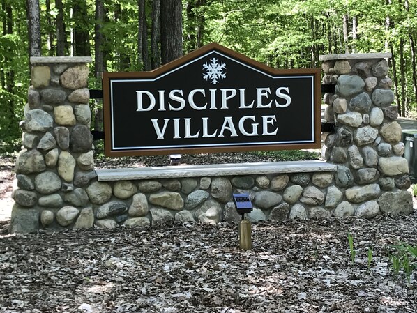 Señal de Disciples Village con un muro de piedra y un emblema de copo de nieve.