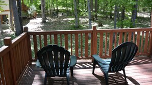 Une terrasse en bois avec deux chaises et une table, entourée d’arbres.