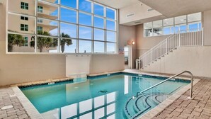 Una piscina interior con agua azul cristalina, un solárium con baldosas y una escalera que conduce a un nivel superior.