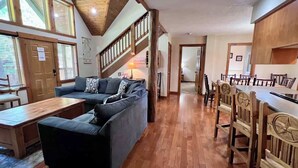A spacious living area with a wooden staircase, a sofa, a dining table, and chairs.