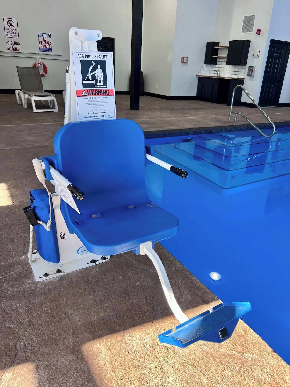 A pool area with a blue pool lift, a sign warning about the pool lift, and a small kitchen area with a sink and cabinets.