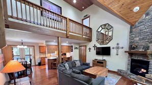 A spacious living area with a large sofa, a fireplace, a balcony, and a kitchen in the background.