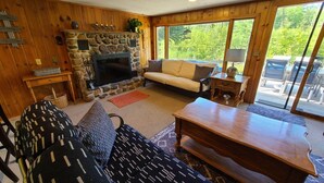 A cozy living room with a stone fireplace, a sofa, a coffee table, and a television. - River Ranch Rental - Cabin in the woods--fishing, relaxation, wildlife, river (Irons)