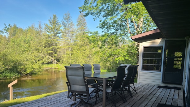 A wooden deck with a table and chairs overlooking a pond, surrounded by trees. - River Ranch Rental - Cabin in the woods--fishing, relaxation, wildlife, river (Irons)