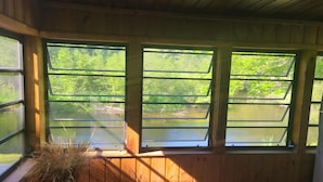 A room with wooden walls and large windows overlooking a body of water and greenery. - River Ranch Rental - Cabin in the woods--fishing, relaxation, wildlife, river (Irons)