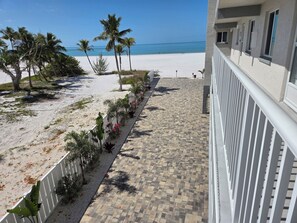 A balcony with a view of a beach and ocean, a tiled walkway, and a white railing.